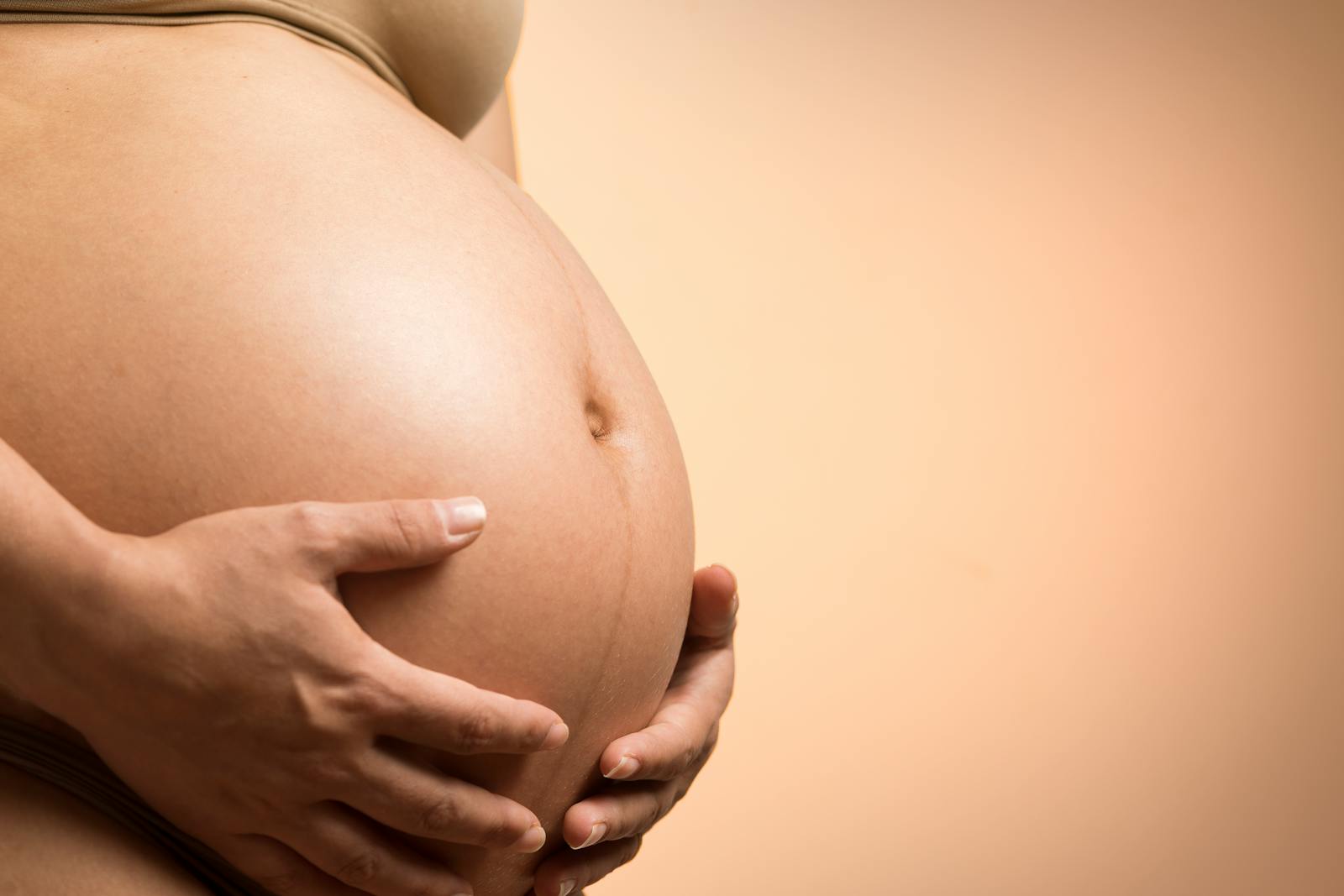 A tender close-up of a pregnant woman's hands holding her belly, symbolizing maternity and love.
